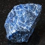 macro shooting of natural rock specimen - rough Sodalite gemstone on black granite background